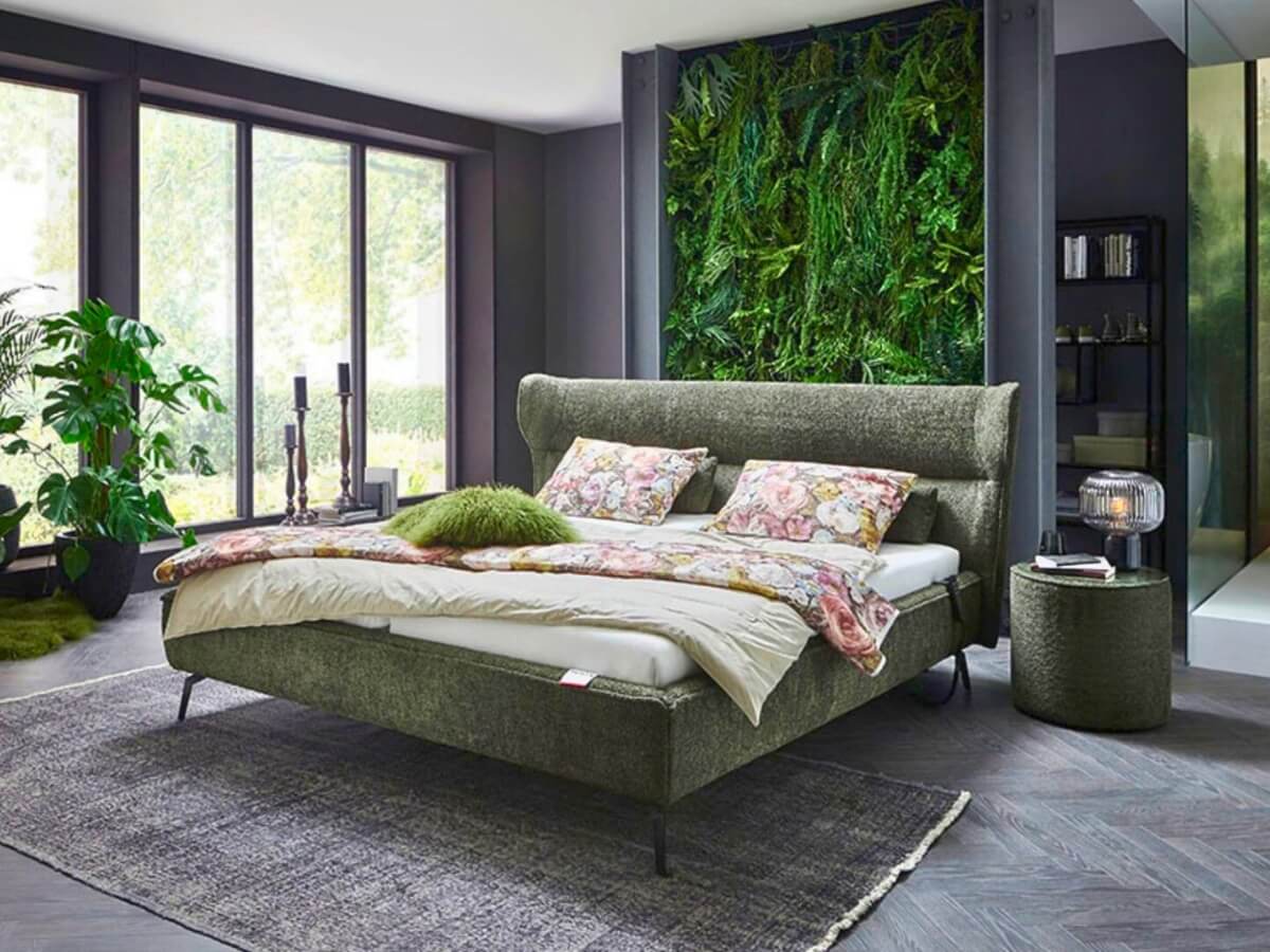 Tmavá spálňa s čalúnenou posteľou a rastlinami.